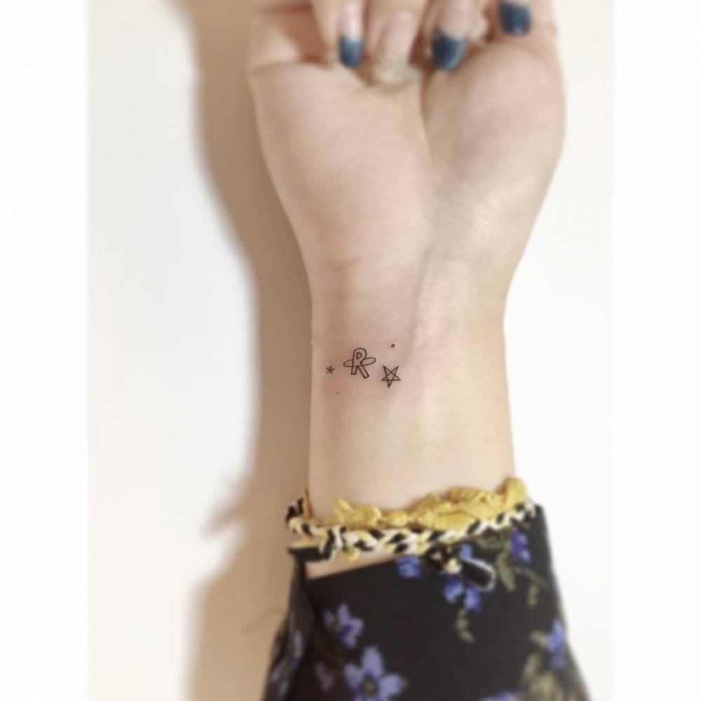 Minimalistic star and letter "R" tattooed on the wrist.