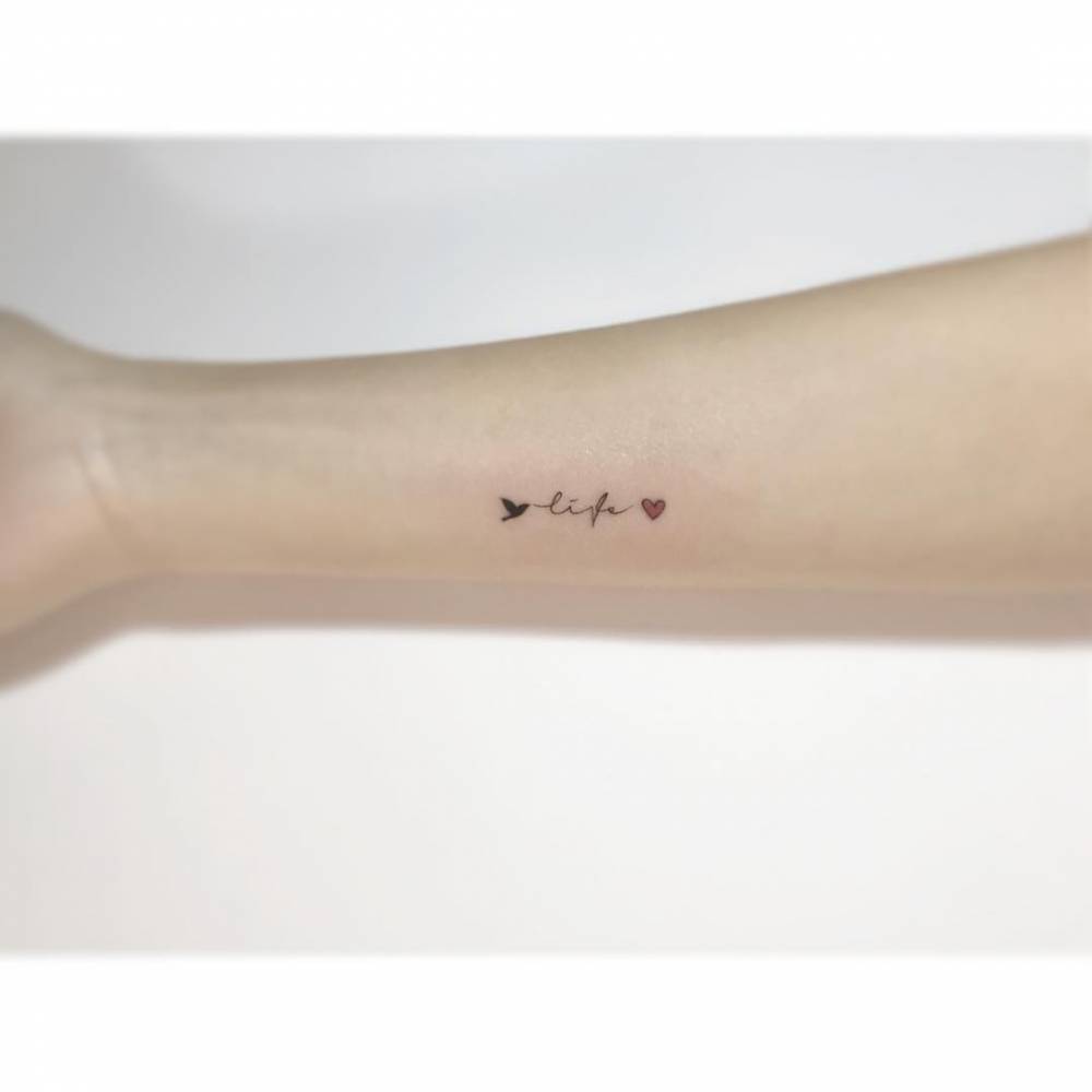 Handwritten font word "life", hummingbird and heart tattooed on the inner forearm.