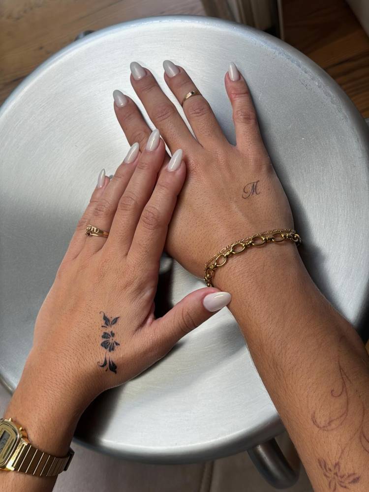 Blackwork style flowers and script font "M" tattooed on the hands
