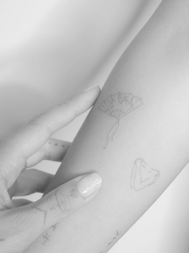 Fine line style hand fan and self hug tattoo located on the inner forearm.