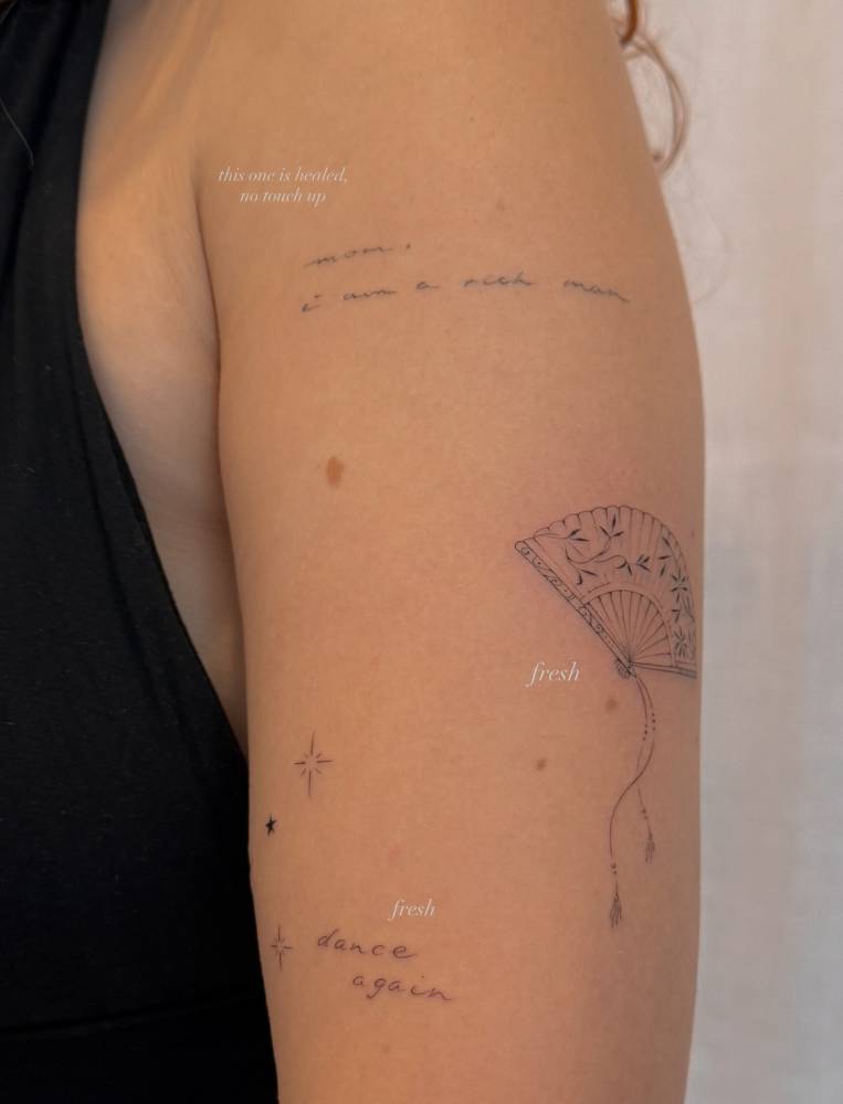 Hand fan and "dance again" tattoos located on the upper arm.