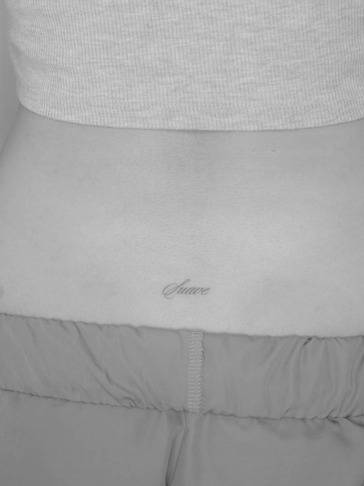 Script font word "suave" tattooed on the lower back.