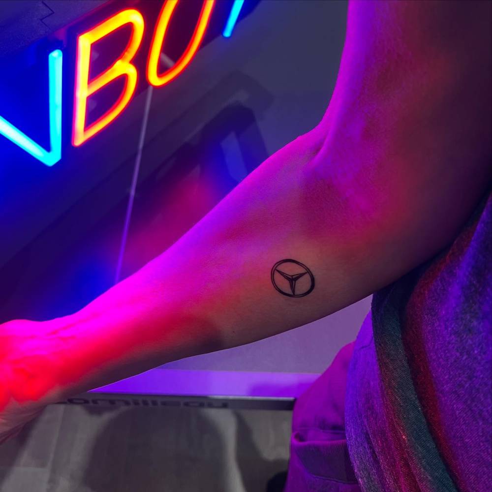 Mercedes-Benz logo tattooed on the inner forearm.
