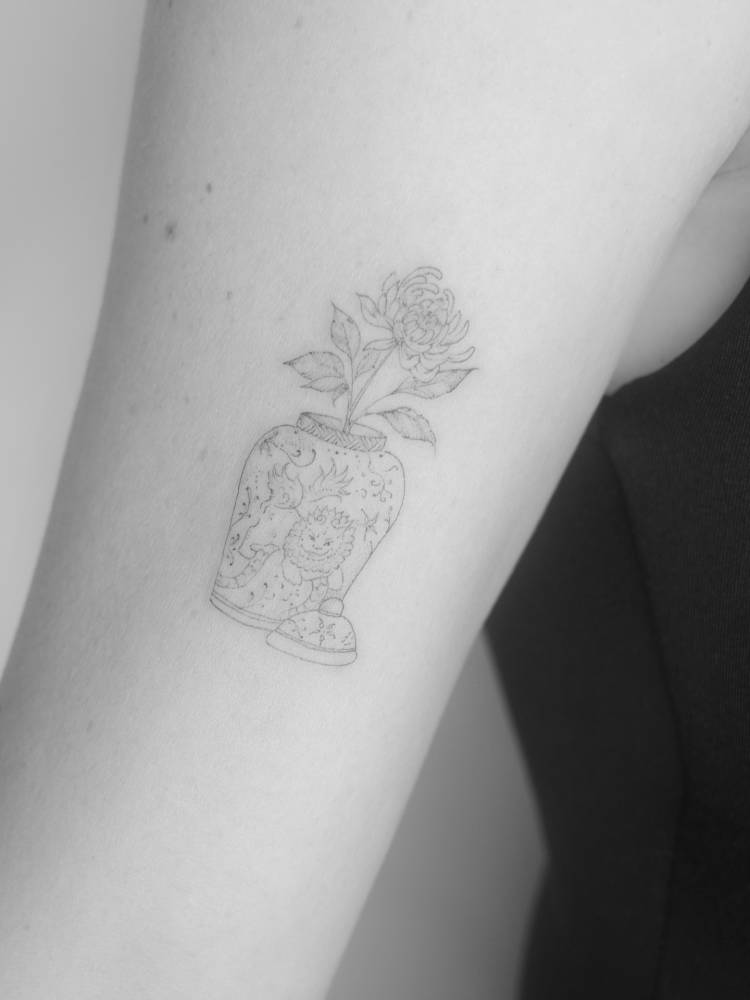 Vase and chrysanthemum tattoo located on the upper arm, fine line style.