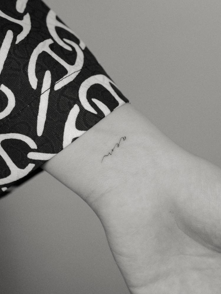 Script font iny initials tattoo located on the wrist.