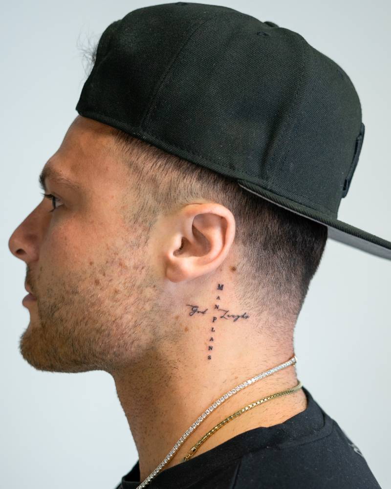 "Man plans, God laughs" lettering cross tattooed on the neck.