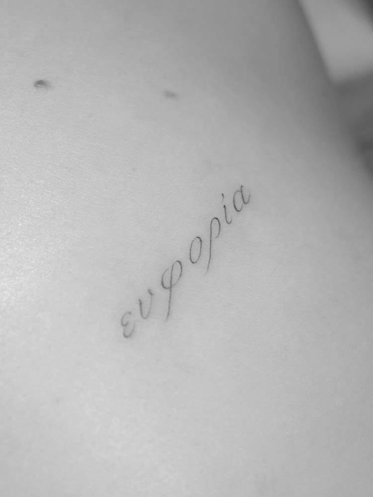 "Ευφορία" lettering tattoo located on the upper arm.