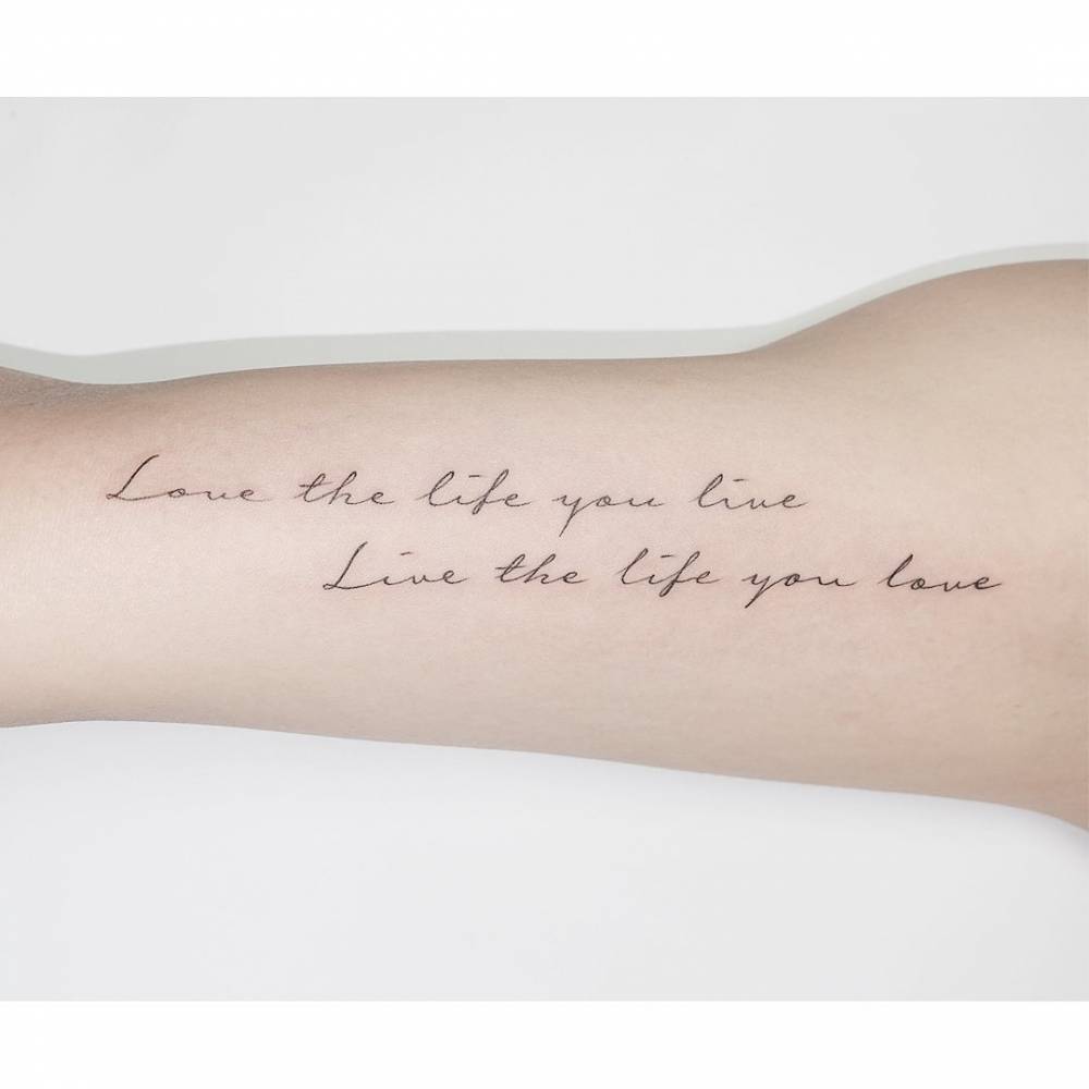 "Love the life you live, live the life you love" lettering tattoo located on the inner arm.