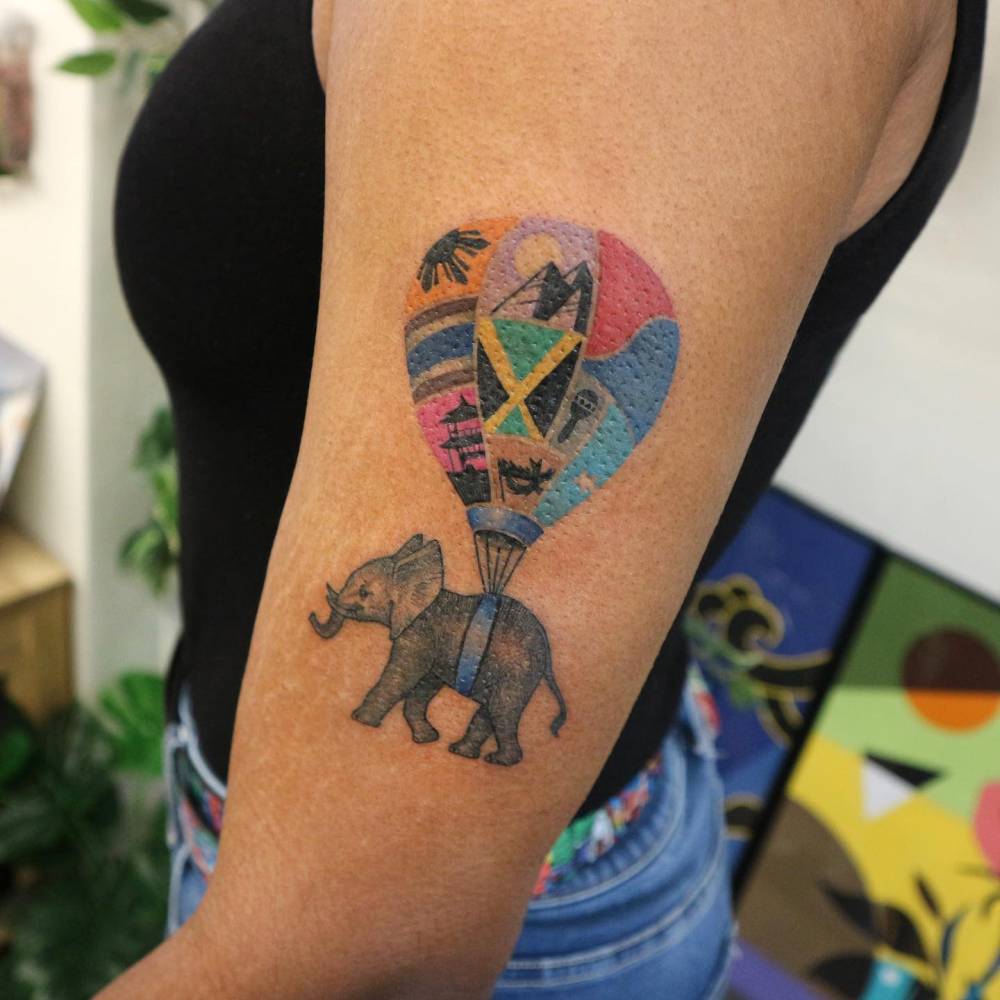 Illustrative style hot air balloon and elephant tattoo located on the upper arm.