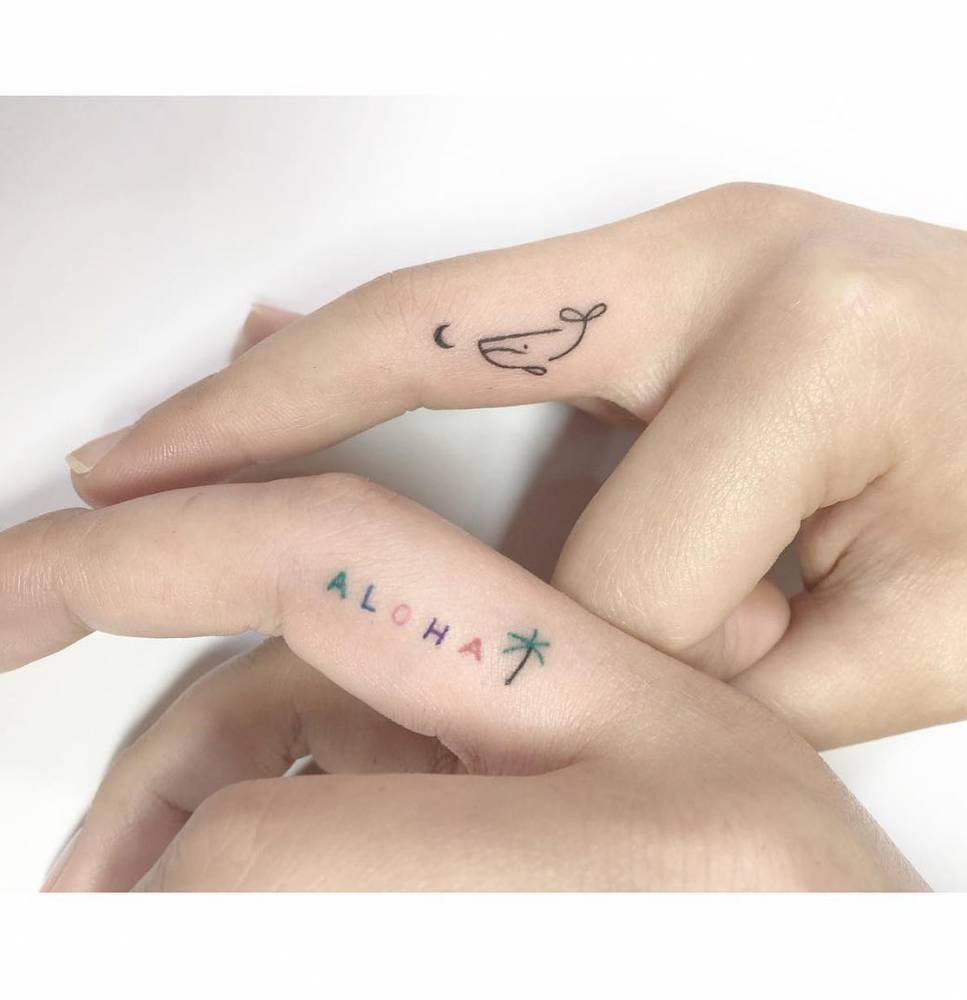Word "aloha" with palm tree and mini whale tattoos located on the fingers.
