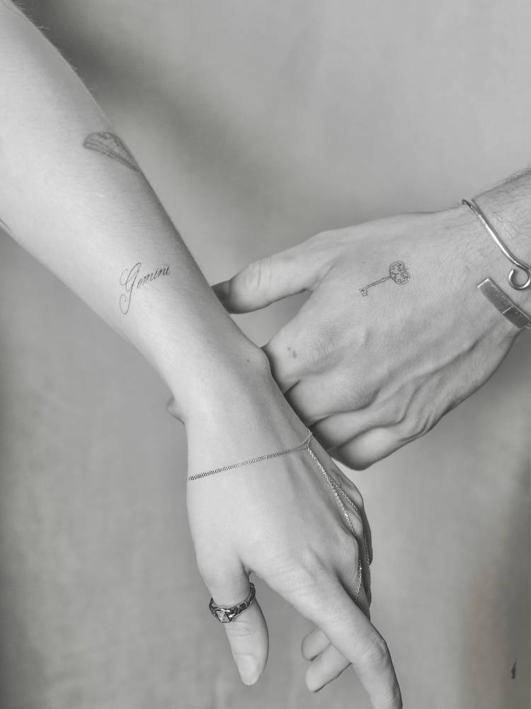 Word "Gemini" and little key tattoos in fine line style.
