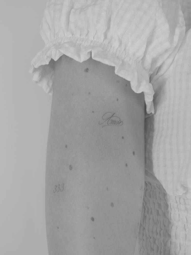 Script font word "amor" tattoo placed on the upper arm.