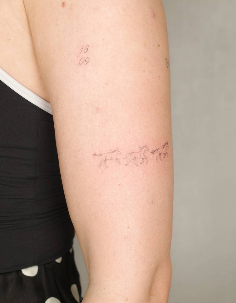 Fine line style little horses tattoo located on the upper arm.