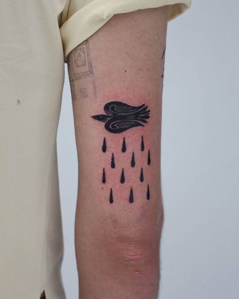 Stylized bird and rain tattoo in blackwork style located on the tricep.
