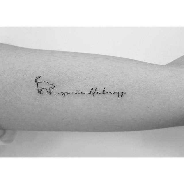 Cat and word "mindfulness" tattoo located on the inner arm.