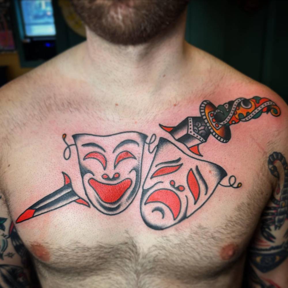 Drama masks and sword tattoo located on the chest, traditional style.