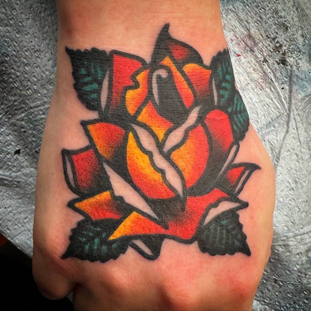 Traditional style orange rose head tattoo placed on the hand.