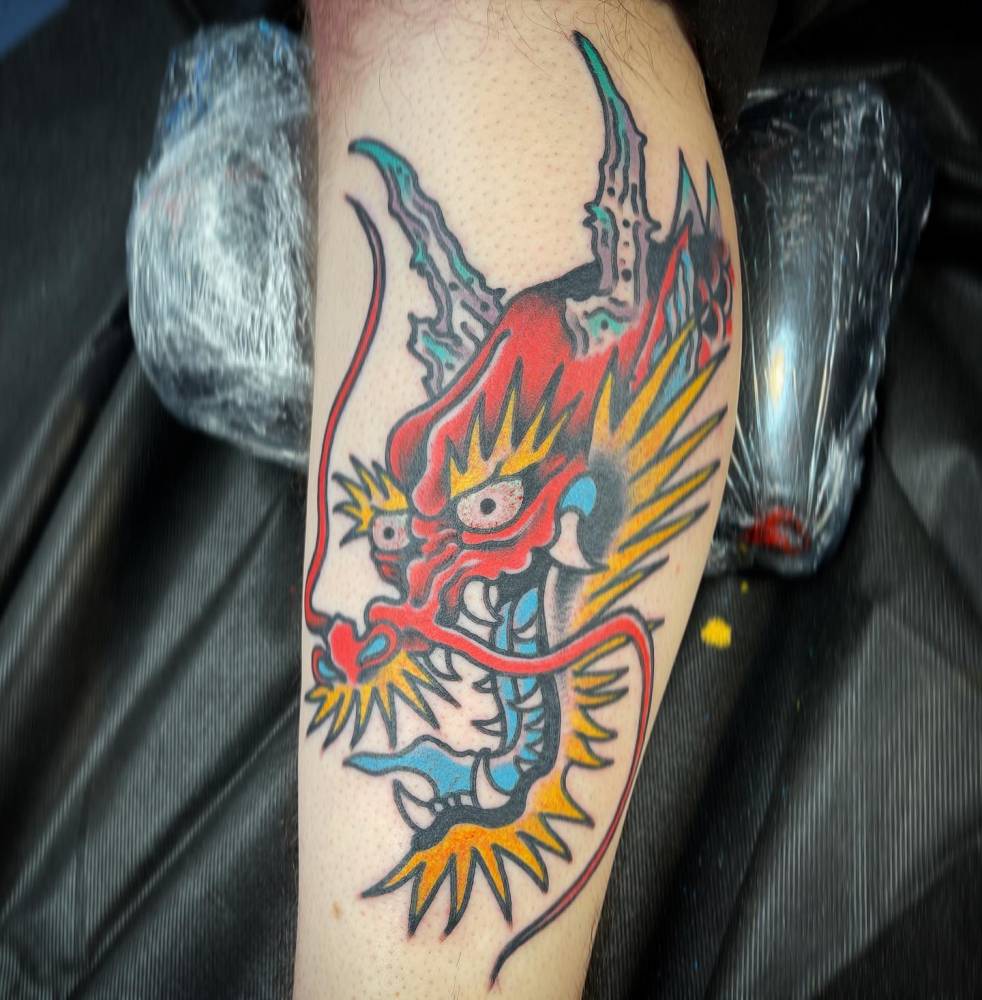Dragon head tattoo in traditional style located on the shin.