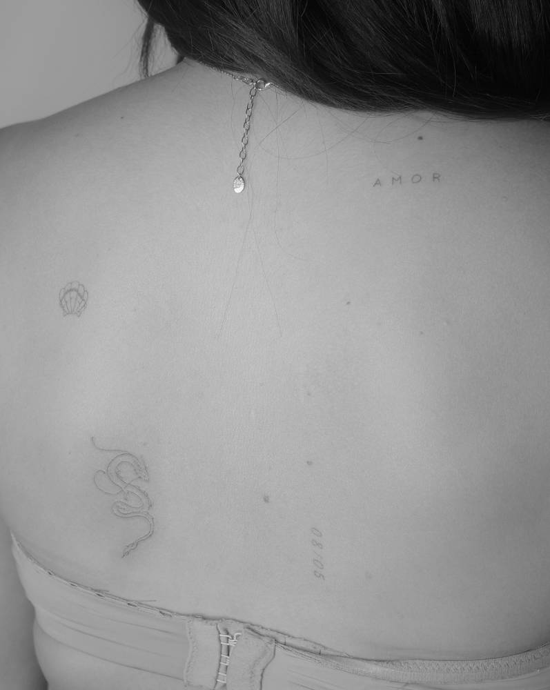Scallop shell, dragon and word "amor" tattoos in fine line style.