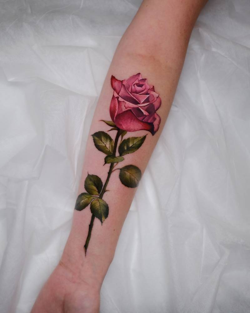 Realistic style pink rose tattoo located on the inner forearm.