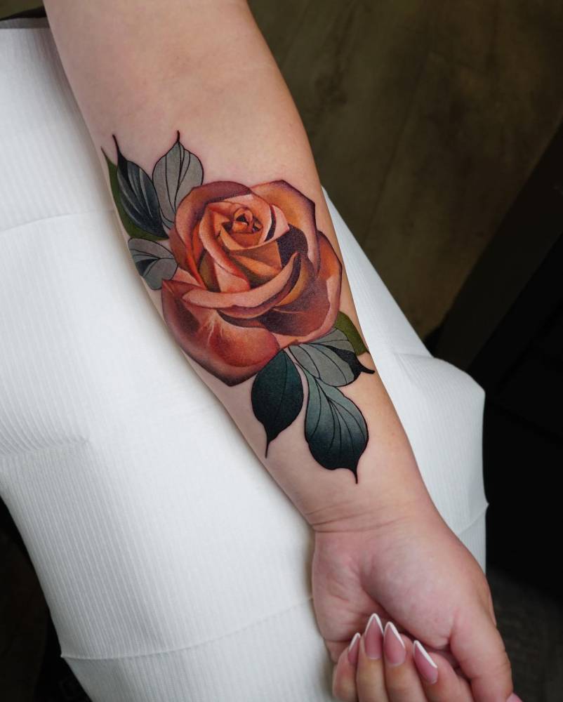 Orange rose head tattoo located on the inner forearm.