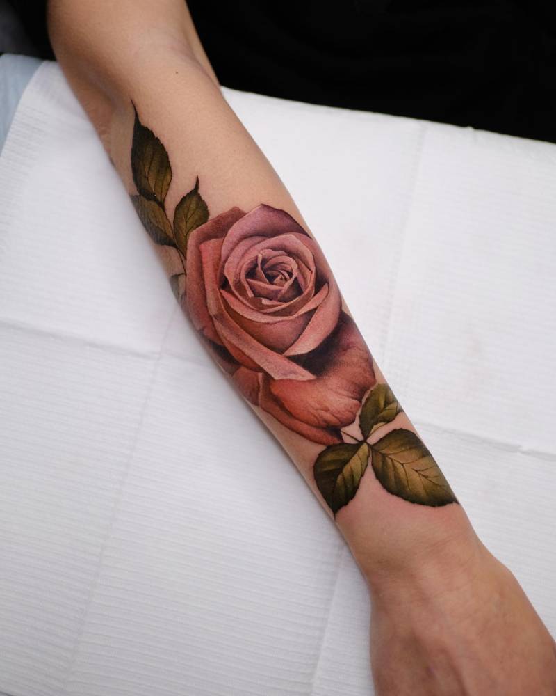 Pink rose tattoo placed on the forearm, realistic style.