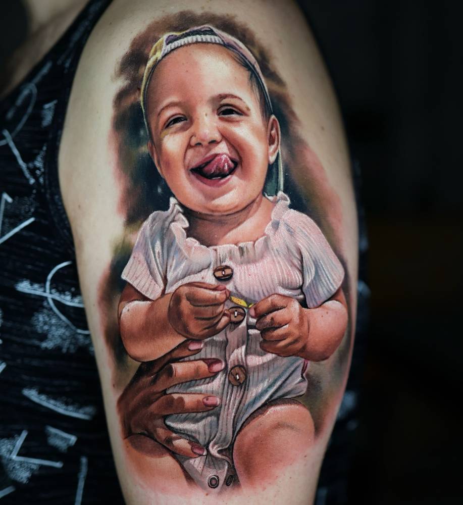 Baby portrait tattoo located on the upper arm, realistic style.