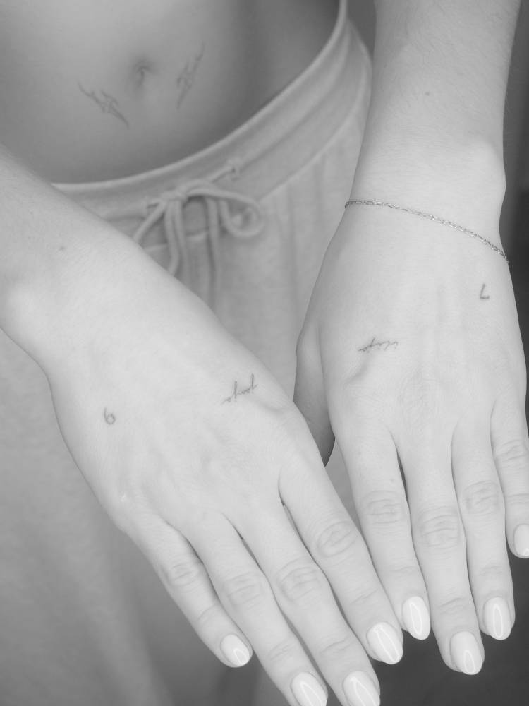 Tiny names in handwritten font tattooed on the hands.