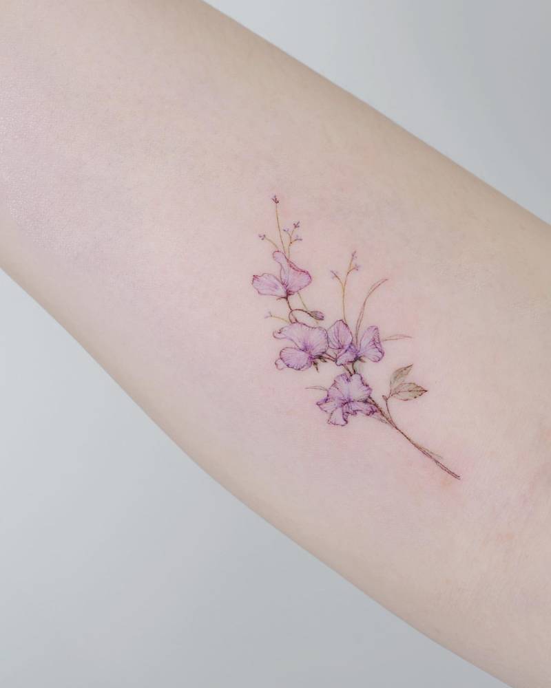 Sweet peas tattoo located on the inner forearm, done in watercolor style.