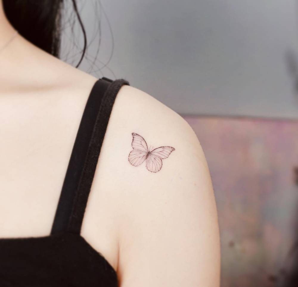 Delicate butterfly tattoo located on the shoulder, illustrative style.