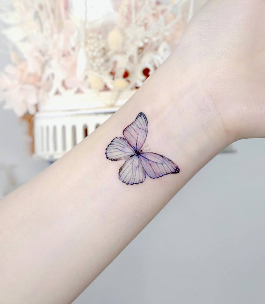 Purple butterfly tattoo located on the wrist, done in watercolor style.