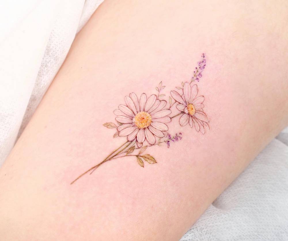 Daisy flowers in watercolor style tattooed on the upper arm.