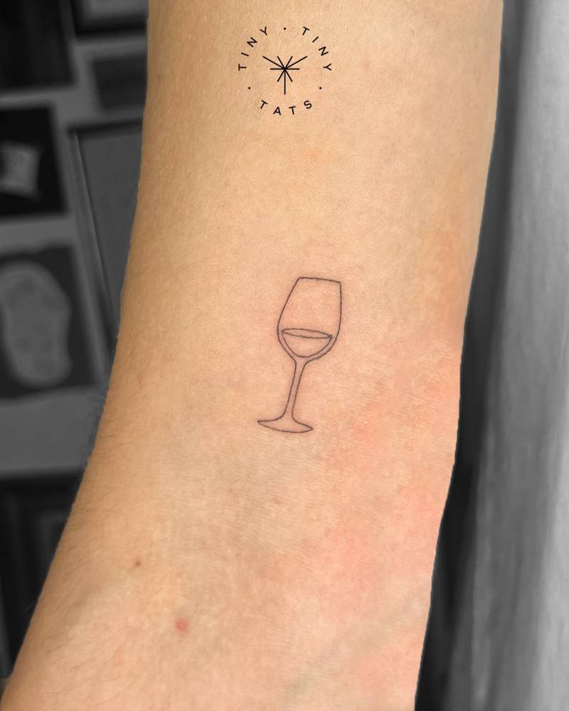 Wine glass tattoo in fine line style located on the bicep.