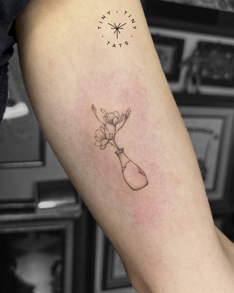 Flowers in a bottle tattoo located on the inner arm, fine line style.