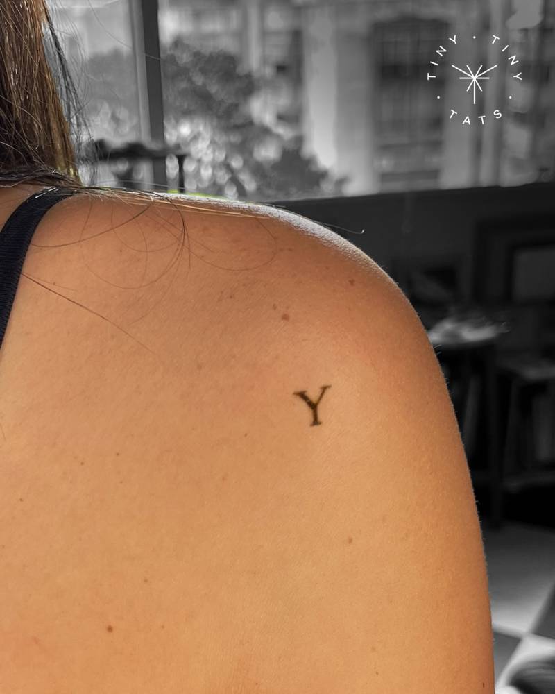 Minimalist letter "Y" in serif font tattooed on the shoulder.