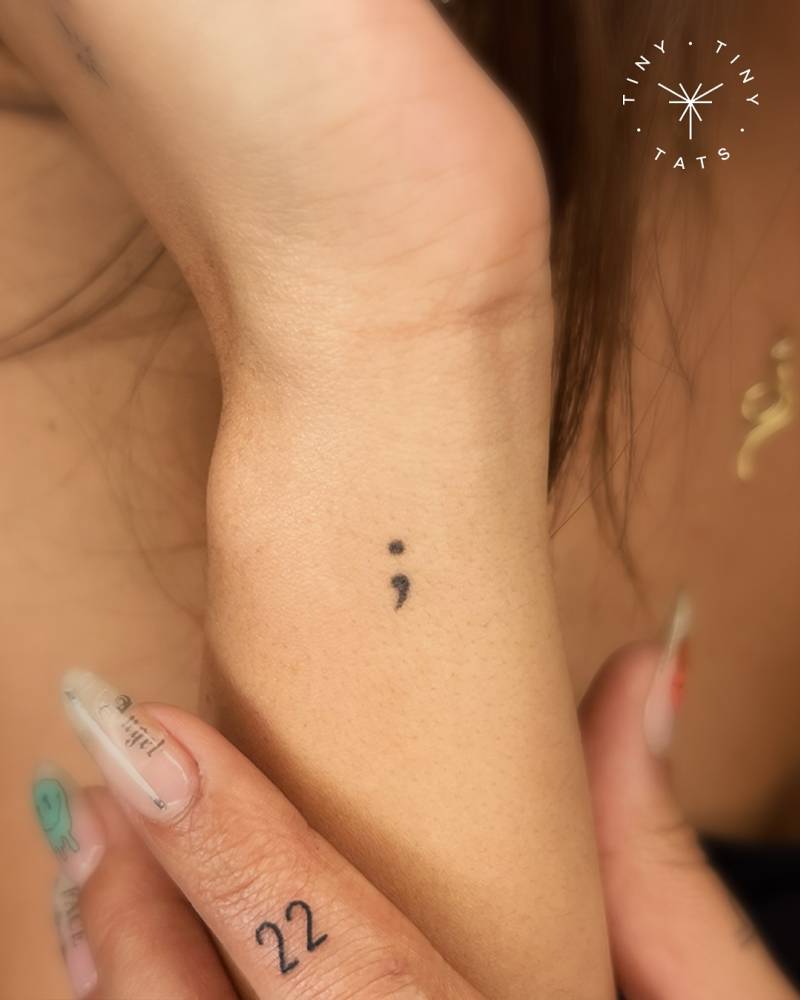 Tiny semicolon and number "22" tattoos in minimalist style.