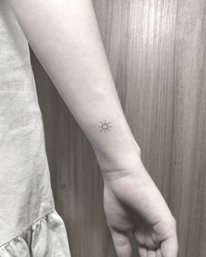 Tiny minimalist sun tattoo located on the wrist.