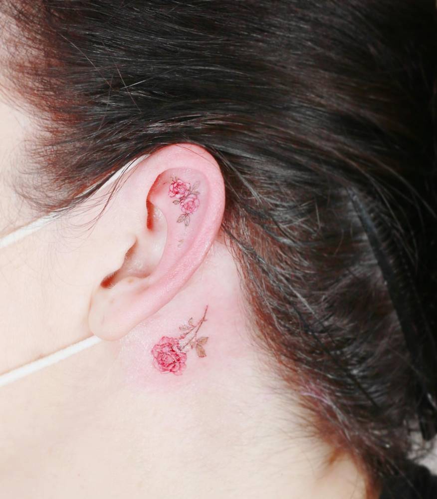 Tiny watercolor style pink rose tattoos placed on and behind the ear.