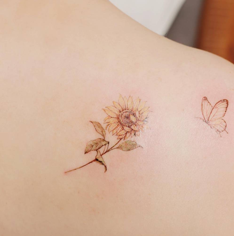 Sunflower and butterfly tattoos located on the shoulder blade, watercolor style.