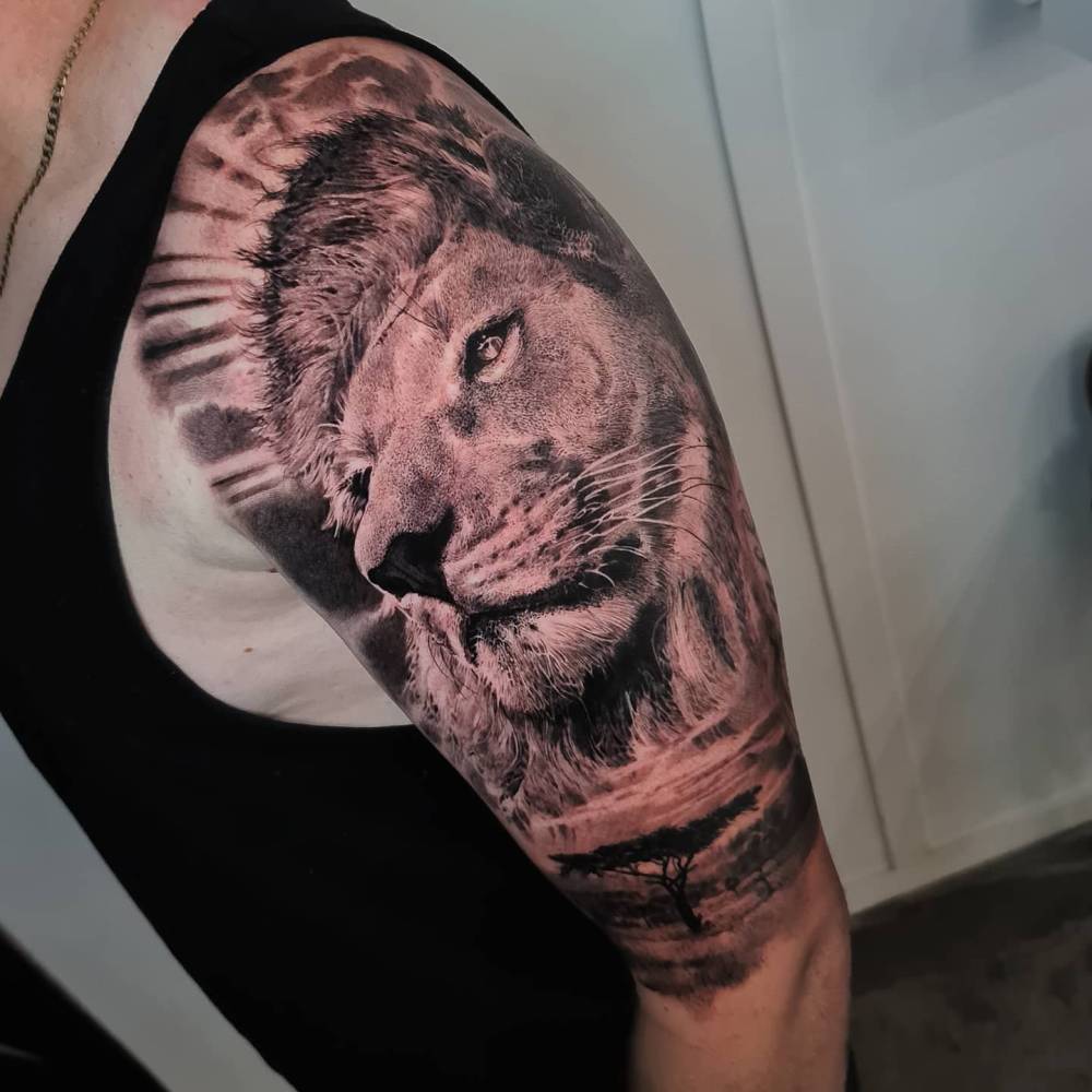 Black and grey style lion portrait tattoo located on the upper arm.