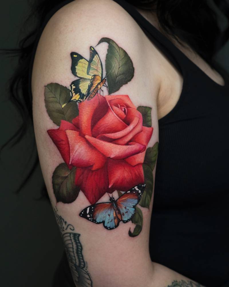 Red rose and butterflies tattooed on the upper arm, realistic style.