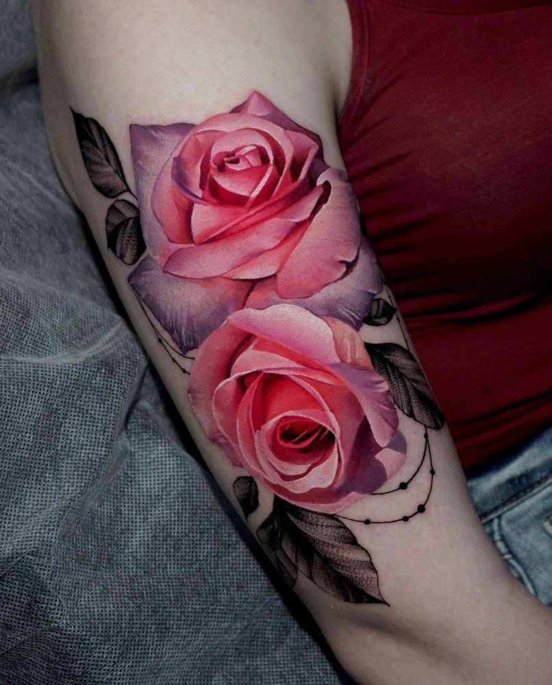 Realistic style pink roses tattoo located on the upper arm.