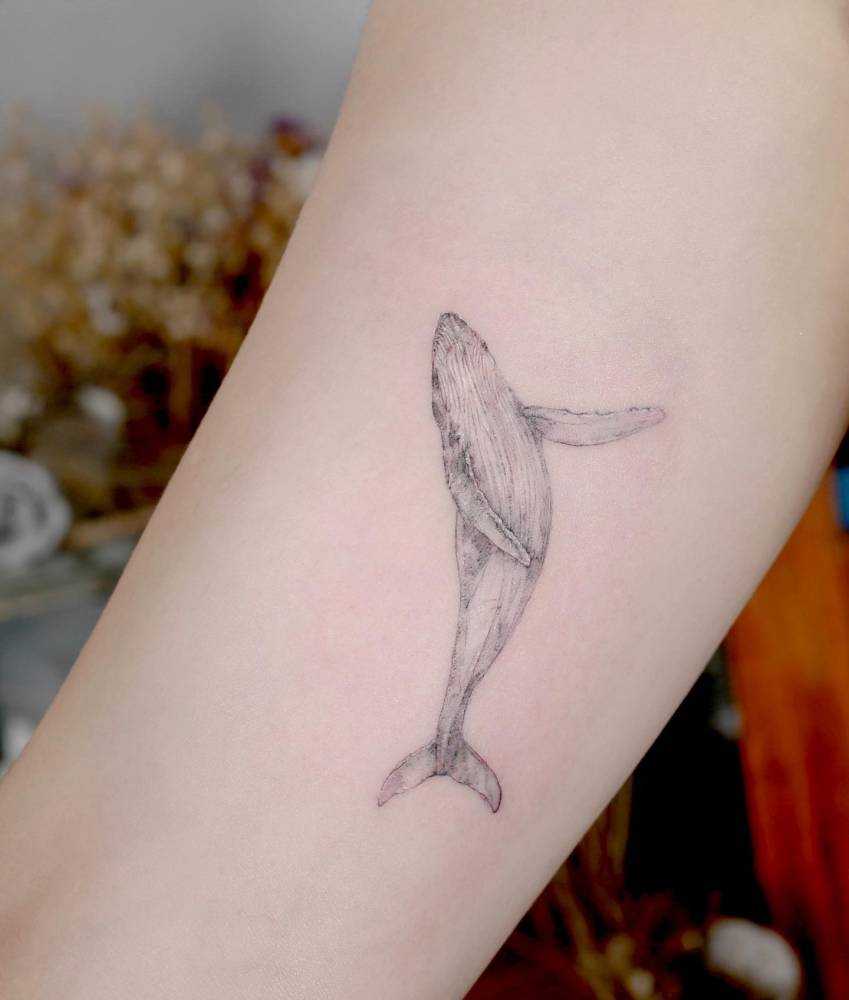 Watercolor style whale tattoo located on the inner arm.