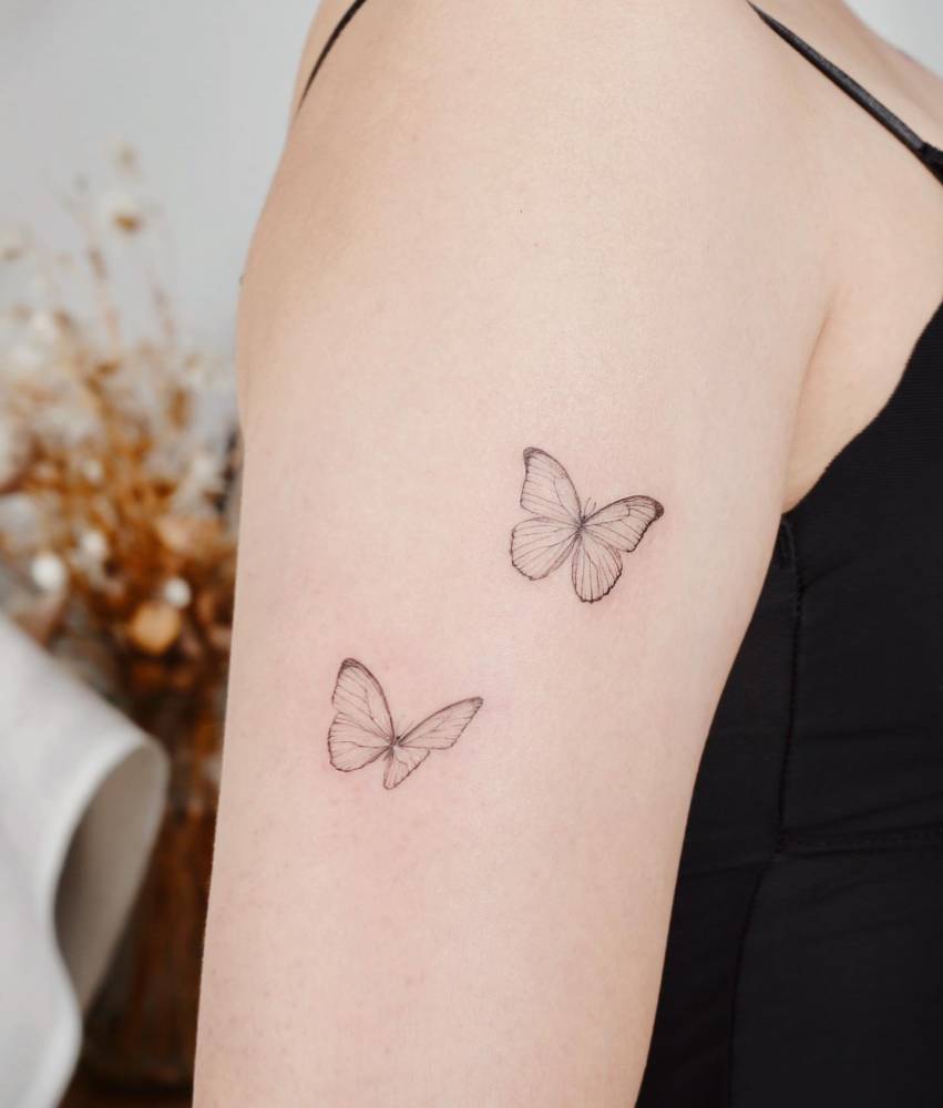 Fine line style butterfly couple tattoo located on the upper arm.