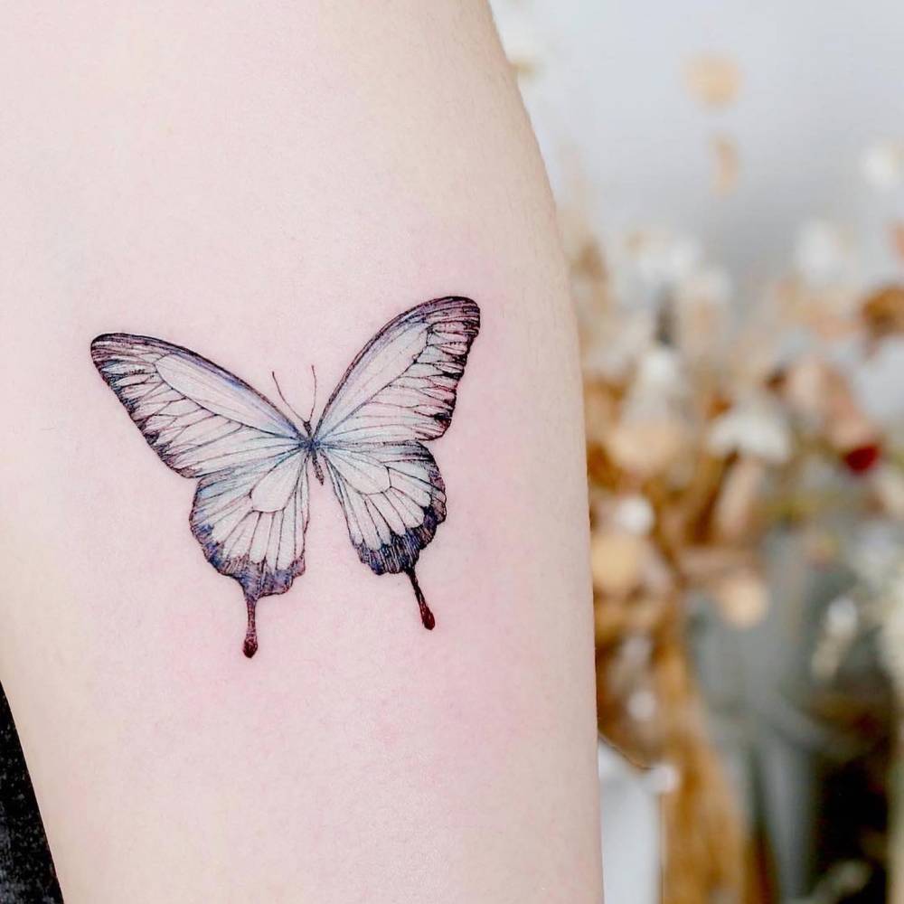 Blue butterfly tattoo in watercolor style located on the upper arm.