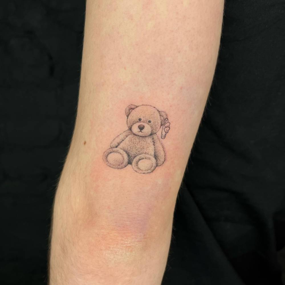 Teddy bear tattoo in illustrative style located on the tricep.