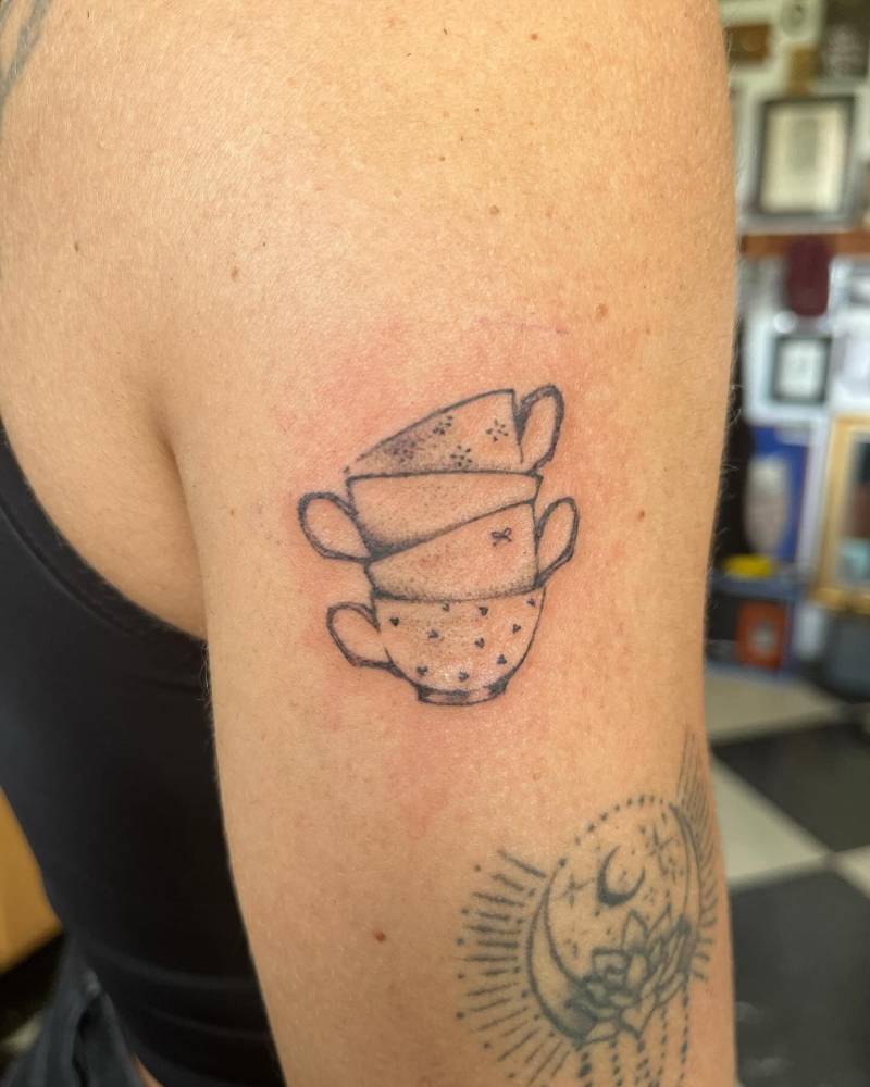 Teacups tattoo in illustrative style located on the upper arm.