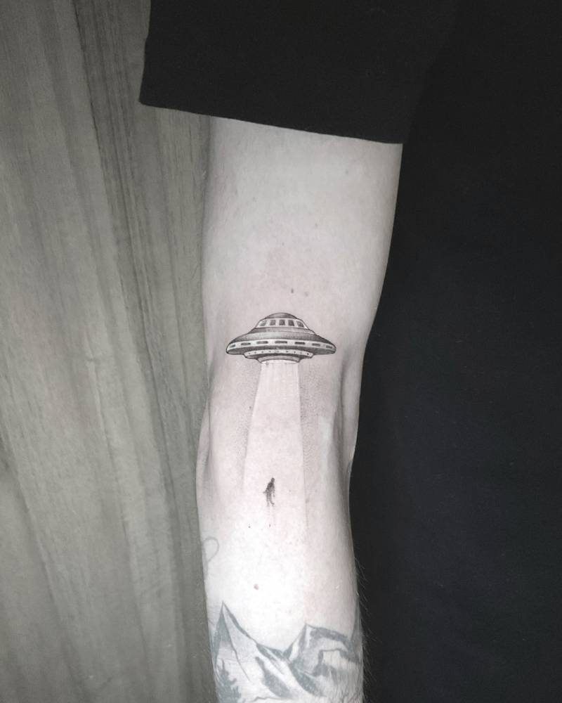 Alien abduction tattoo in  illustrative style located on the elbow.