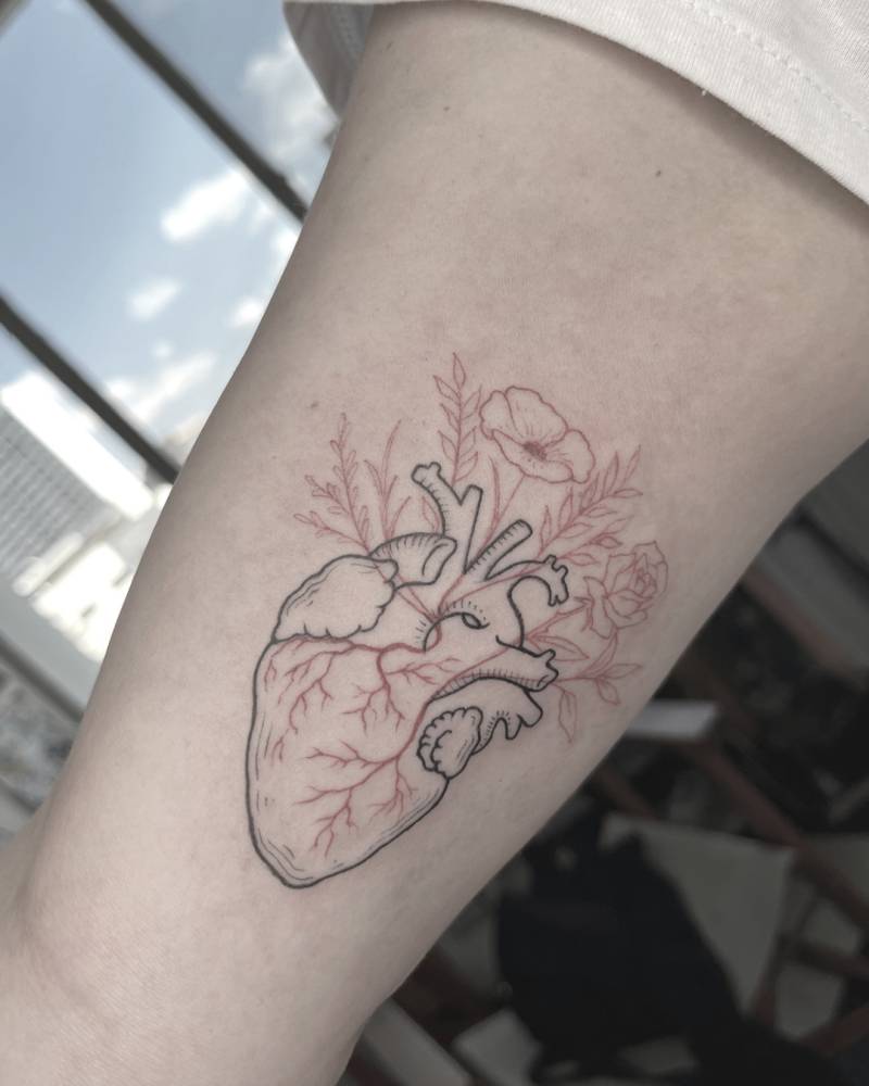 Anatomical heart with flowers tattoo in fine line style located on the inner arm.