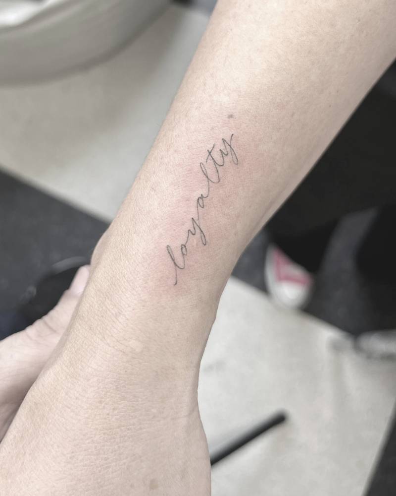 Handwritten font word "loyalty" tattoo placed on the wrist.